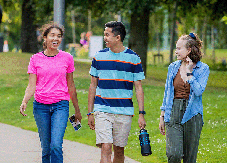 Five students walk together in a grassy campus. One has a bicycle.